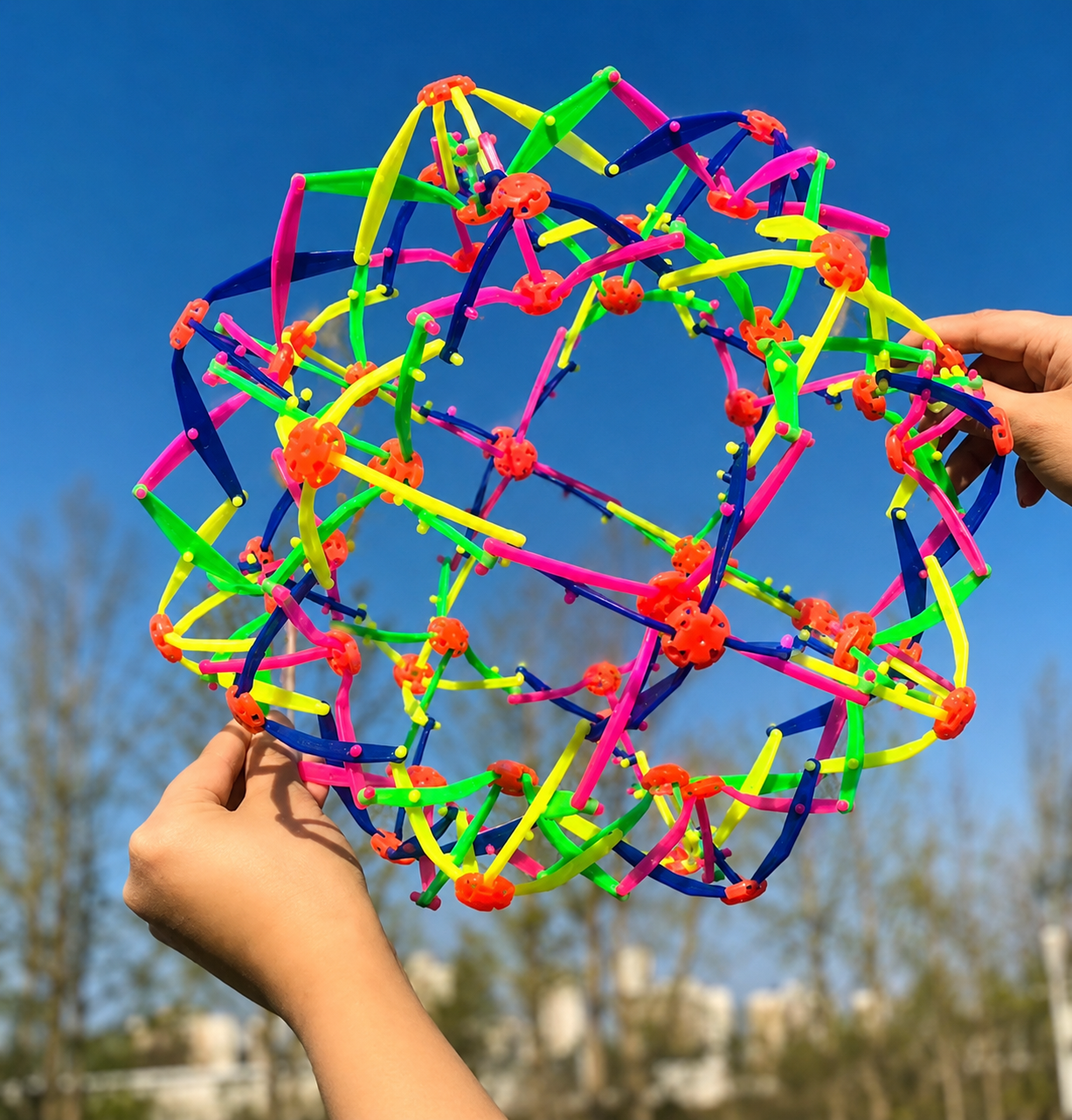 Expandable Ball wird von zwei Händen auseinandergezogen und entfaltet sich zu einer großen bunten Kugel.
