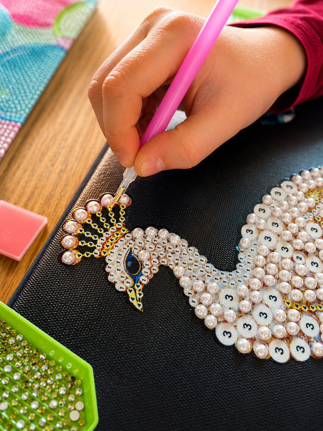 Kind setzt mit dem Diamond-Painting-Stift Glitzersteine auf ein funkelndes Kunstwerk