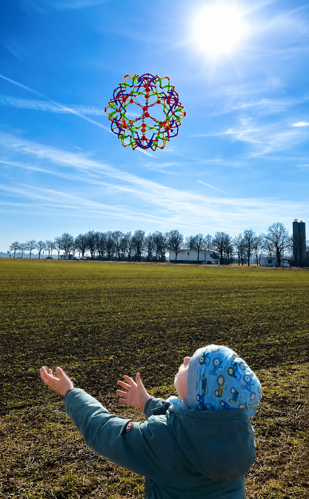 Kind wirft einen Expandable Ball auf einer Wiese in die Luft und beobachtet den Flug.